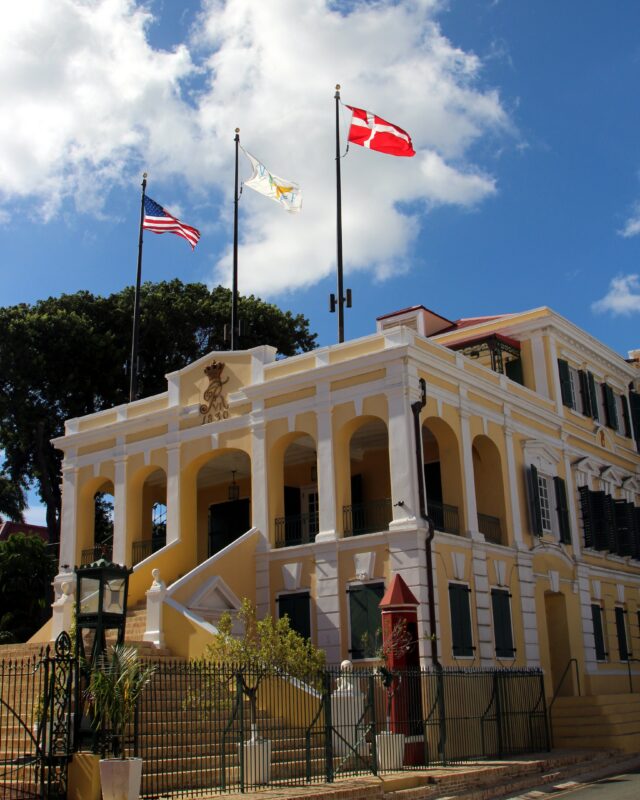 The Government House is a large, beautiful colonial mansion painted yellow with white trim.