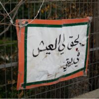 A white and orange poster pined to a metal fence with Arabic writing on it that reads “I have the right to live in my house.”