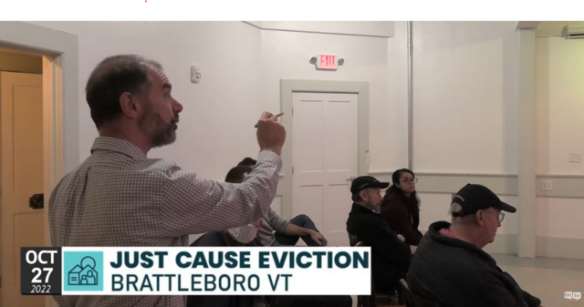  Screen shot from Brattleboro Just Cause Eviction Community Meeting, showing a middle aged man standing up and pointing his finger with a pen in his hand. 