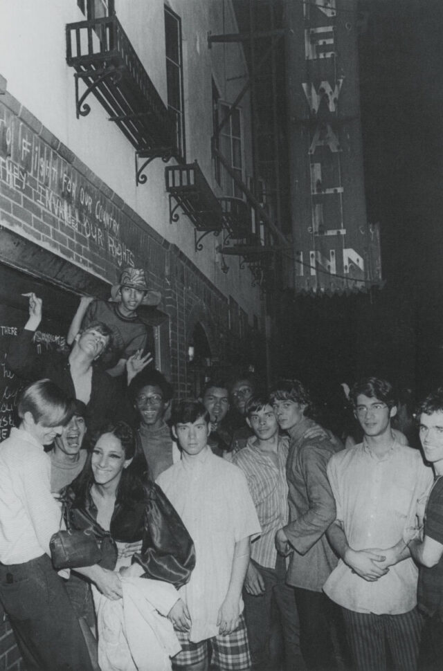 Approximately a dozen people stand outside of the damaged Stonewall Inn shortly after the 1969 Stonewall Riots.