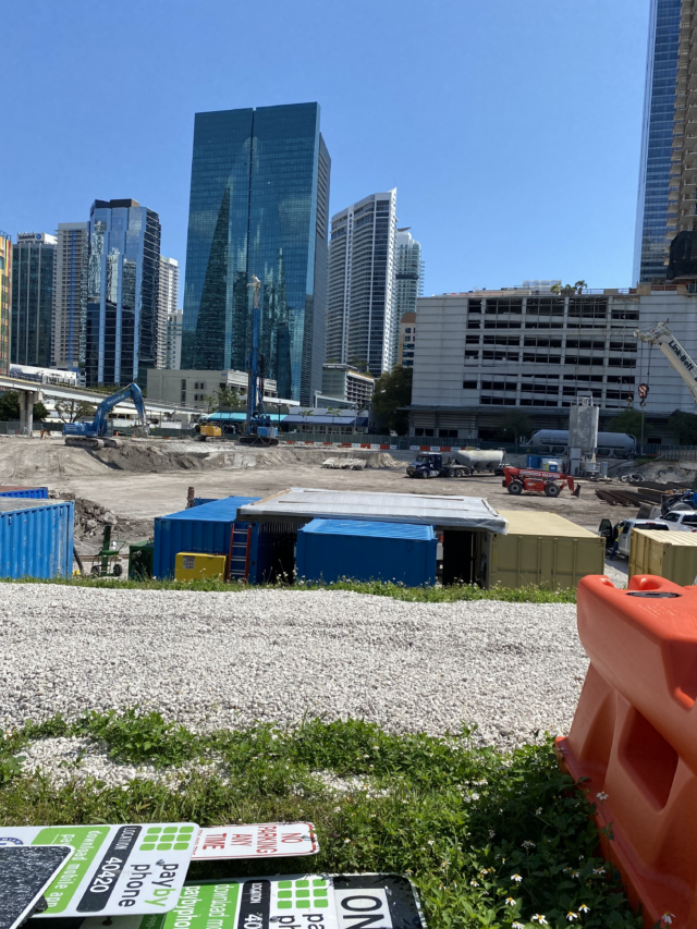 A construction site with a parking garage in the background. The parking garage is about half as tall as the building next to it. 