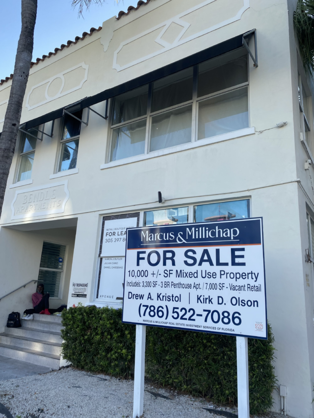 An apartment building with a sign in front of it reading “For Sale,” a sign behind it reads “For Lease.”