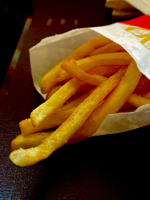 Close-up of golden McDonald’s french fries spilling from a white paper bag onto a dark tray.