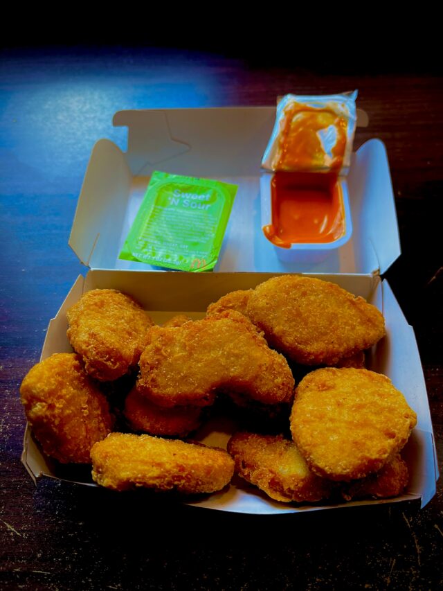 Open McDonald’s box filled with 10 chicken nuggets and two dipping sauces—a green Sweet ’N Sour packet and an opened cup of Spicy Buffalo sauce.