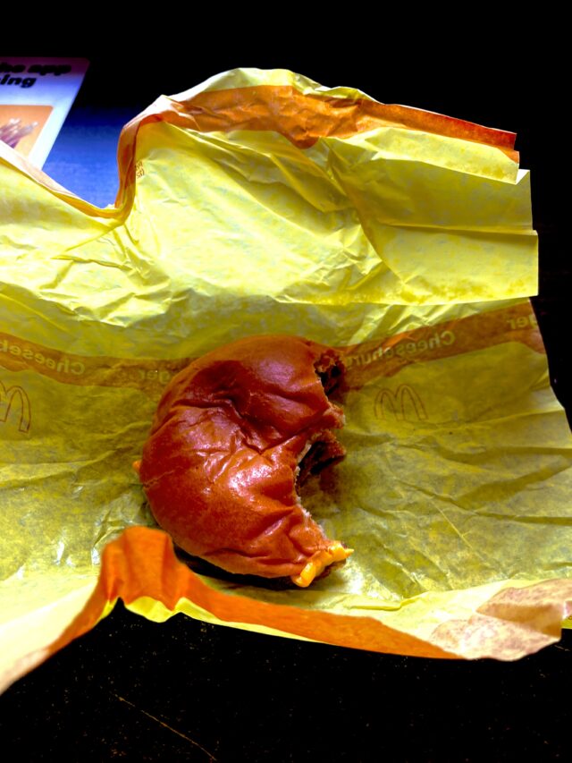 A bitten McDonald’s cheeseburger resting on its opened yellow wrapper.