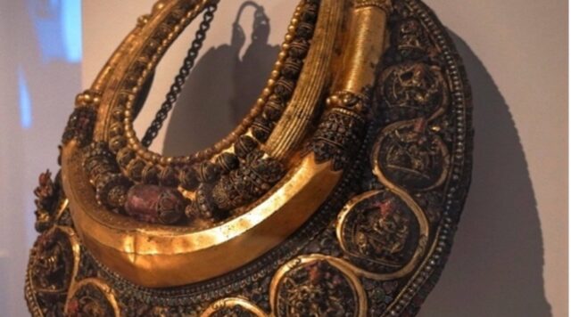 A photograph of the Taleju necklace, a golden necklace with engravings and jewel, in its display case at the Art Institute.