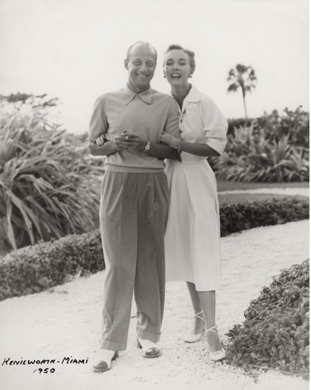 A black and white photograph taken by Kenilworth in Miami in 1950 of James and Marilyn posing together on a walkway surrounded by palm trees, shrubs, and lawns.