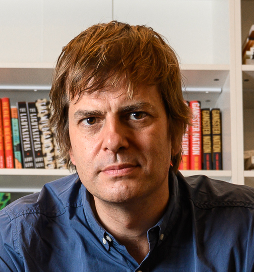 A headshot of a man in front of a bookcase.