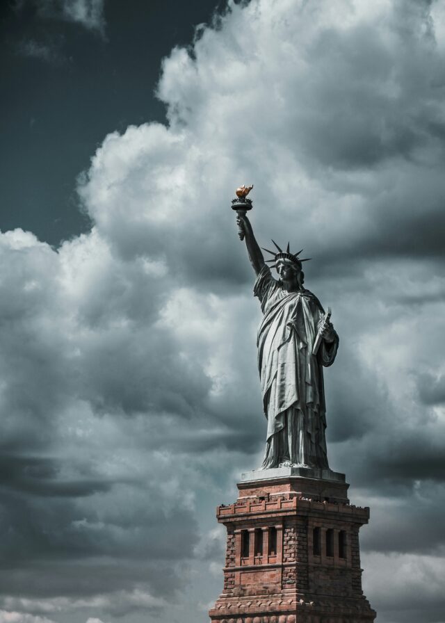 The Statute of Liberty stands in the foreground with storm clouds gathering in the background.