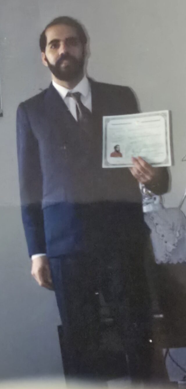 My father, wearing a dark blue suit, stands holding his Certificate of Citizenship. 