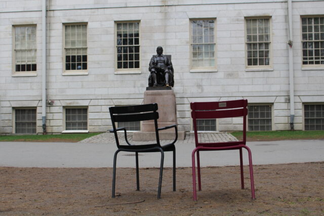The John Harvard statue facing two empty chairs 