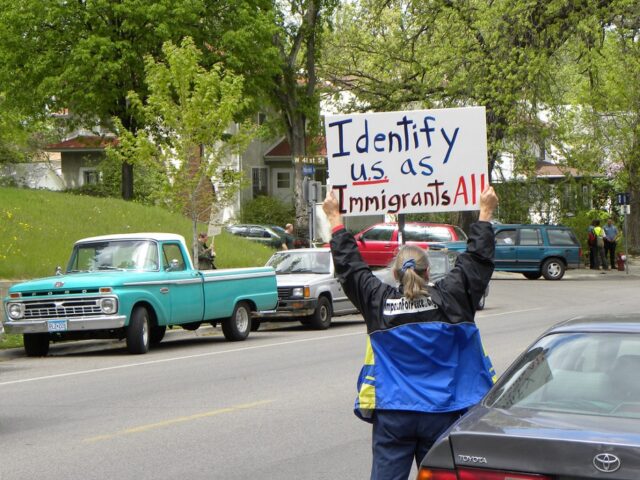 A protestor in Minnesota holding a sign reading “Identify U.S. as Immigrants All.”