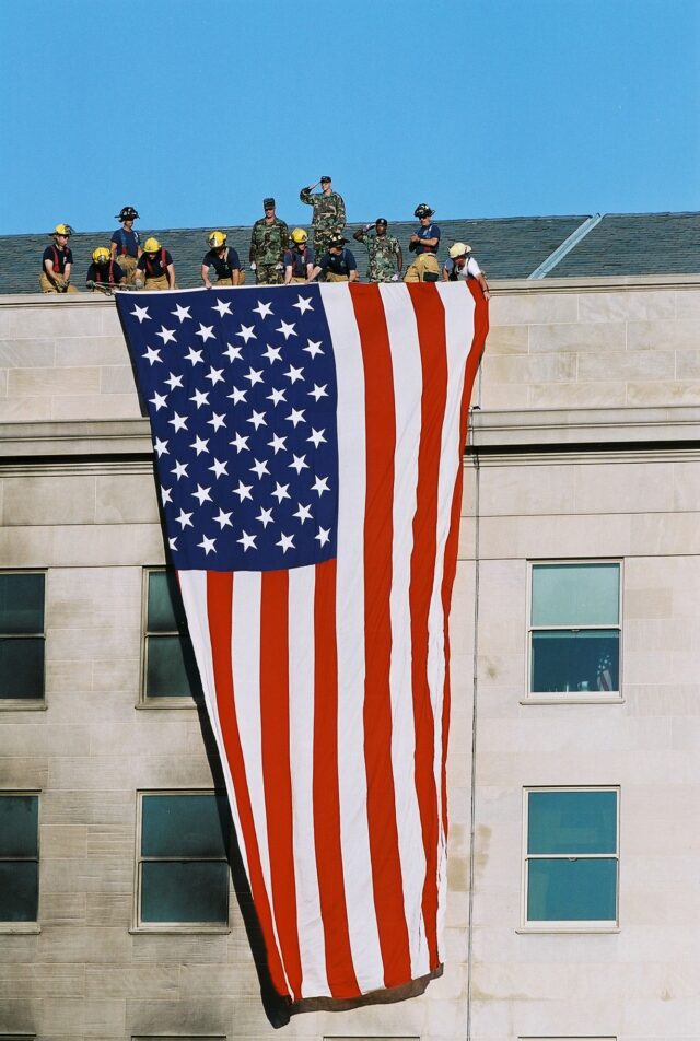 Fire fighters and military personnel unfurl a large American flag from the roof of the Pentagon during President George W. Bush’s visit on September 12, 2001.